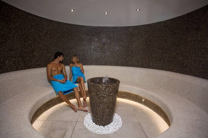 Mūsdienīga Astor Garden spa centra relaksācijas telpa ar mozaīkas sienām, akmens strūklaku un ērtiem sēdekļiem atpūtai