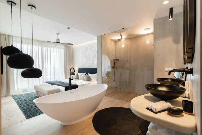 Astor Garden luksusa numurs ar atvērtā plānojuma vannas istabu, brīvstāvošu vannu, melnām izlietnēm un skatu uz guļamzonu
