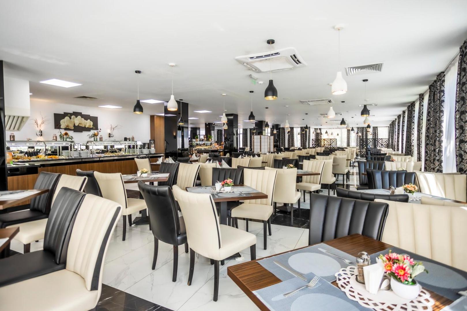Prestige Deluxe Hotel Aquapark Club plašais restorāns ar bufetes zonu, gaišām mēbelēm un modernu apgaismojumu
