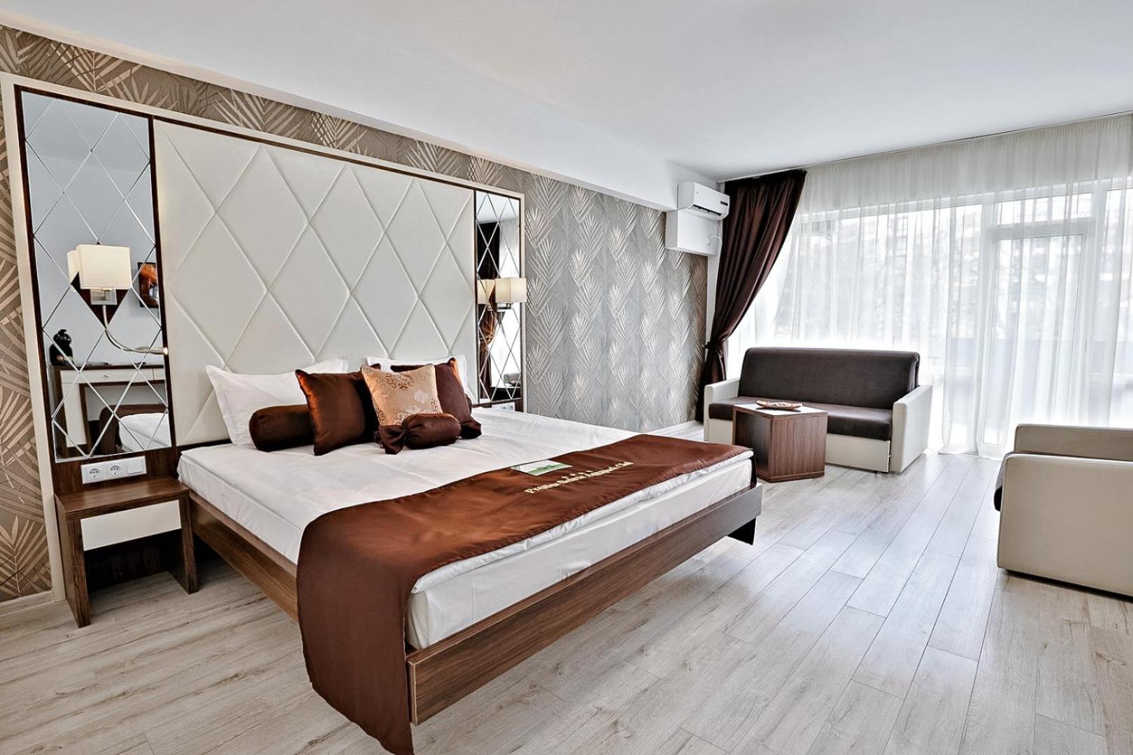 Prestige Deluxe Hotel Aquapark Club numurs ar dekoratīvām tapetēm, brūniem akcentiem tekstilā, lielu spoguli un mīksto mēbeļu zonu