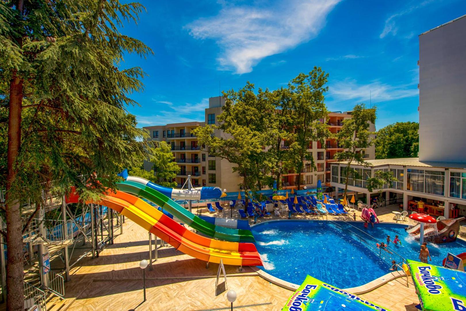 Prestige Deluxe Hotel Aquapark Club akvaparka zona ar lielajiem slidkalniņiem un sauļošanās krēsliem koku ieskāvumā