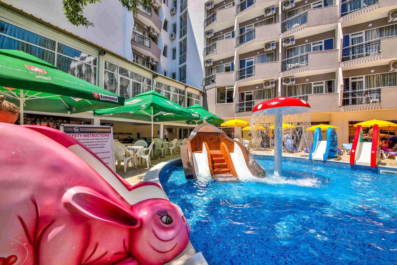 Bērnu baseins ar sēnes formas strūklaku un slidkalniņiem pie Prestige Deluxe Hotel Aquapark Club ēkas fasādes Zelta Smiltīs.