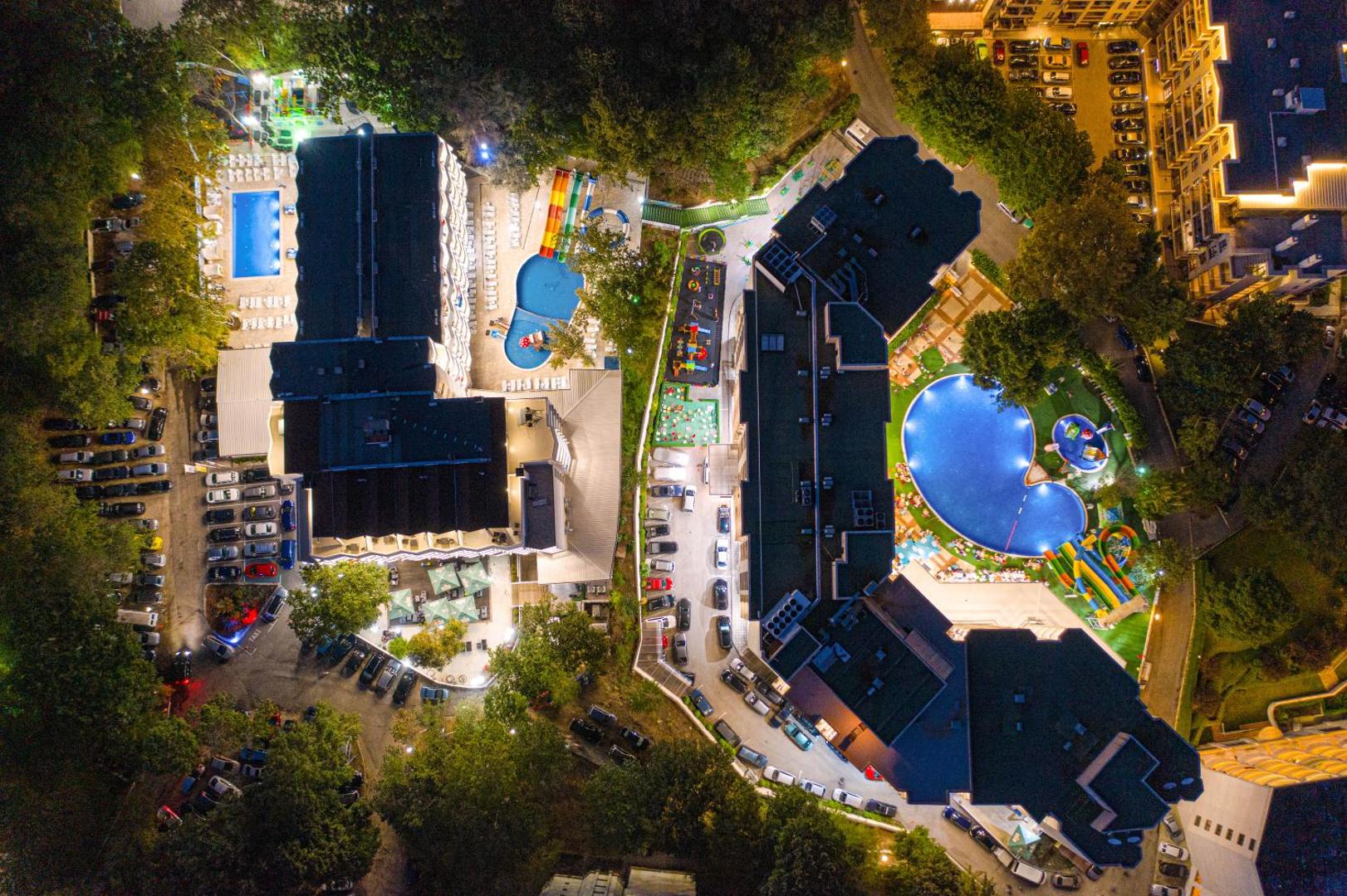 Prestige Deluxe Hotel Aquapark Club skats no putna lidojuma naktī — izgaismoti baseini, ūdens slidkalniņi un viesnīcas korpusi Zelta Smiltīs, Bulgārijā
