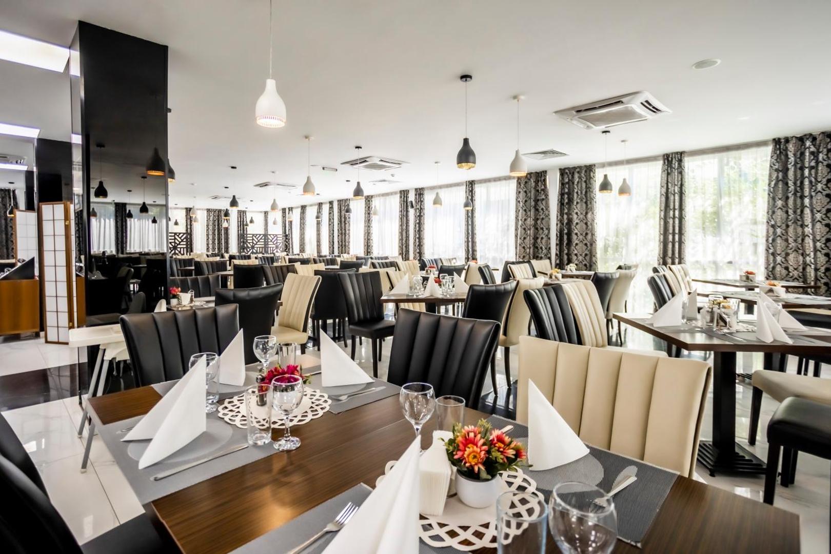 Prestige Deluxe Hotel Aquapark Club restorāna zāle ar klātiem galdiem, dekoratīviem ziediem un elegantiem aizkariem