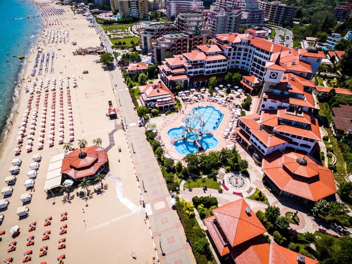 Helena Sands kūrorta panorāmas skats uz baseinu zonu un piekrastes promenādi — redzama pludmale ar saulessargiem un viesnīcas arhitektūra