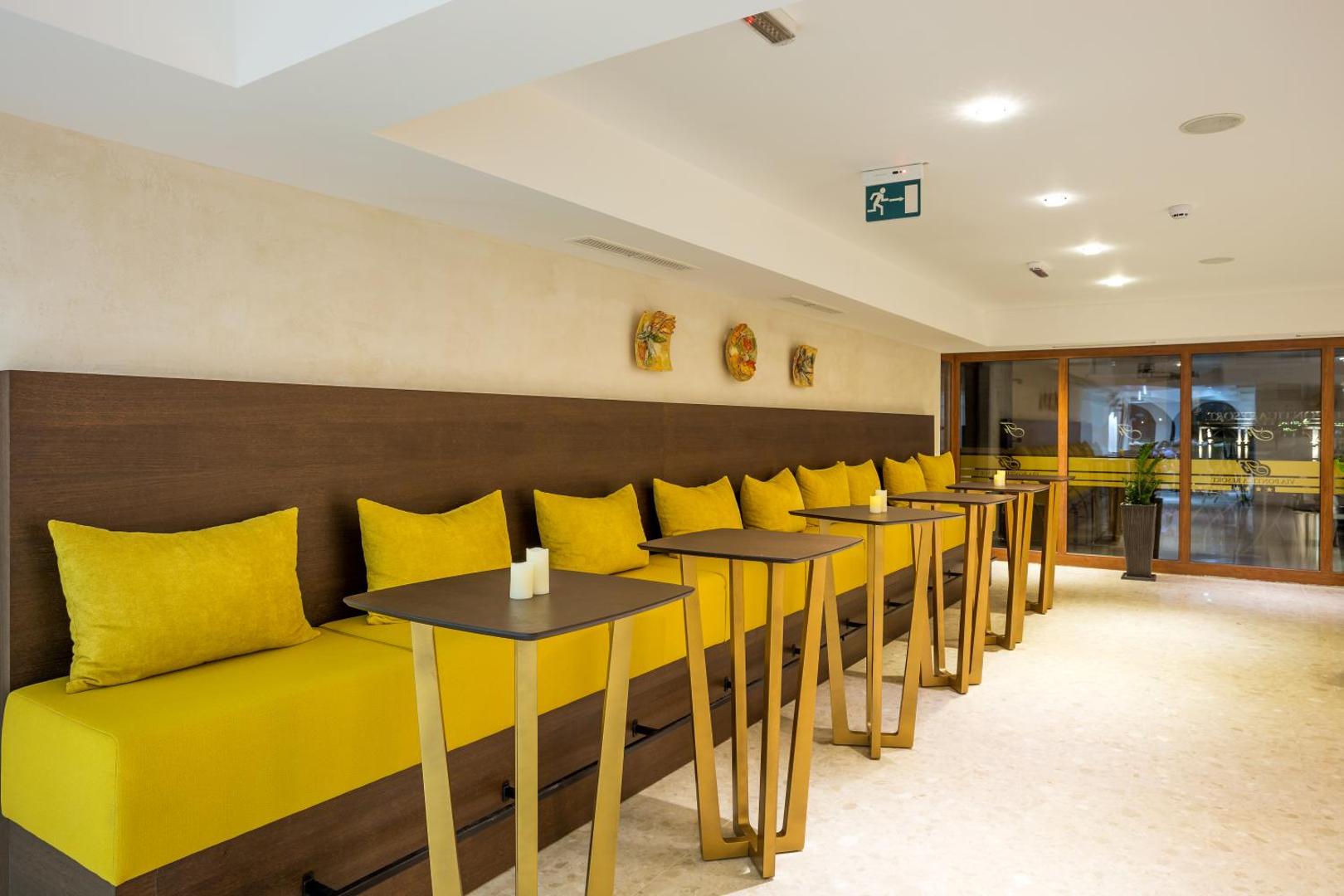 Festa Via Pontica Resort atpūtas zona ar dzelteniem dīvāniem un augstajiem galdiem, radot mājīgu atmosfēru viesiem