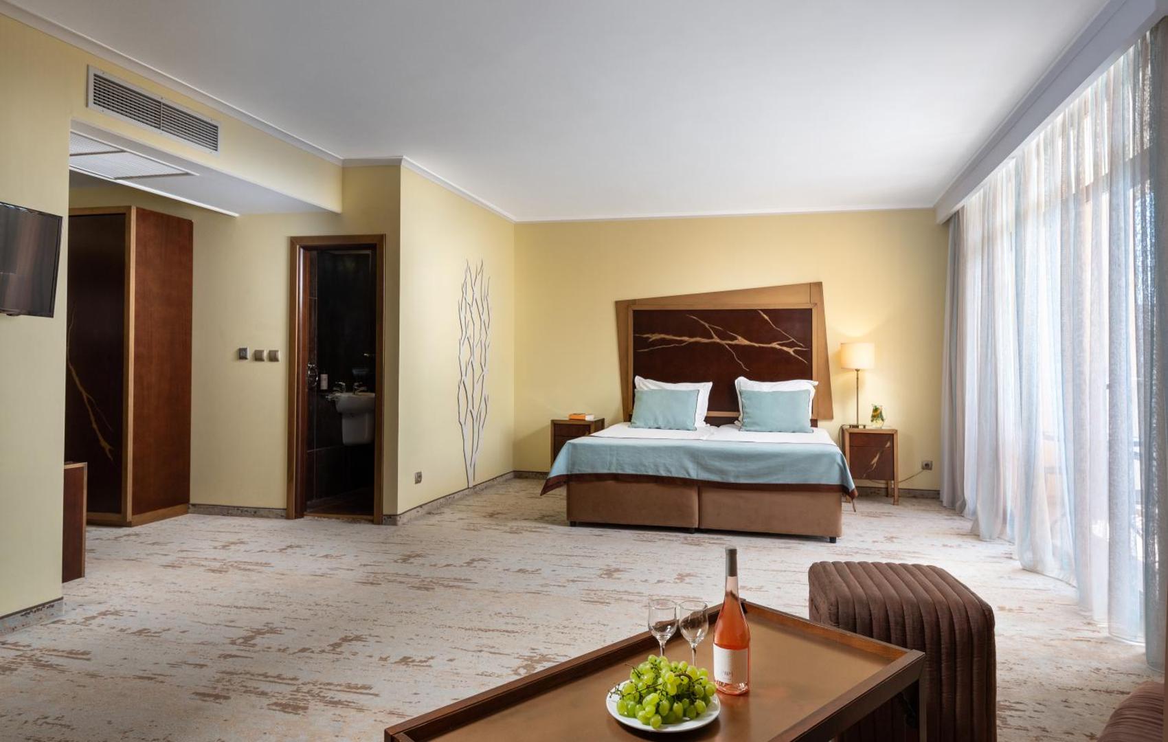Festa Via Pontica Resort plašs luksusa numurs ar atpūtas zonu, vīnu un augļiem uz galda — skats uz guļamzonu