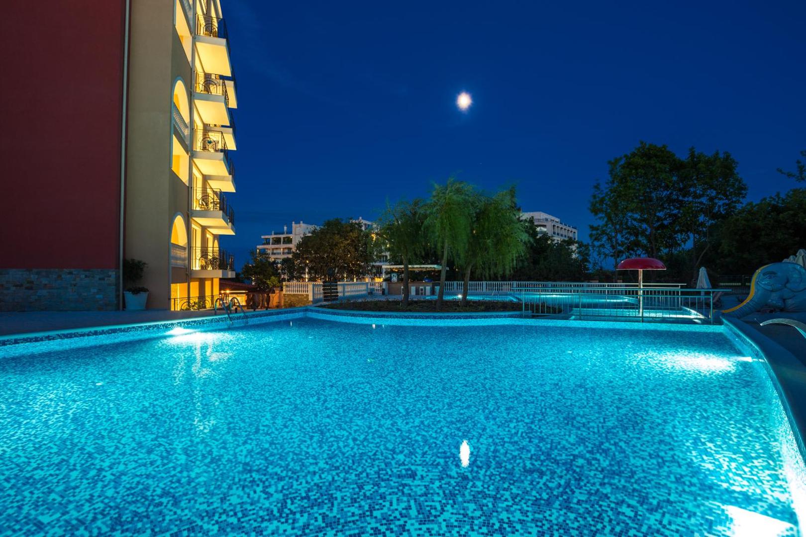 Festa Via Pontica Resort baseina zona nakts laikā ar mēness gaismu un bērnu atrakcijām Pomorijā — mierīga nakts ainava kūrortā