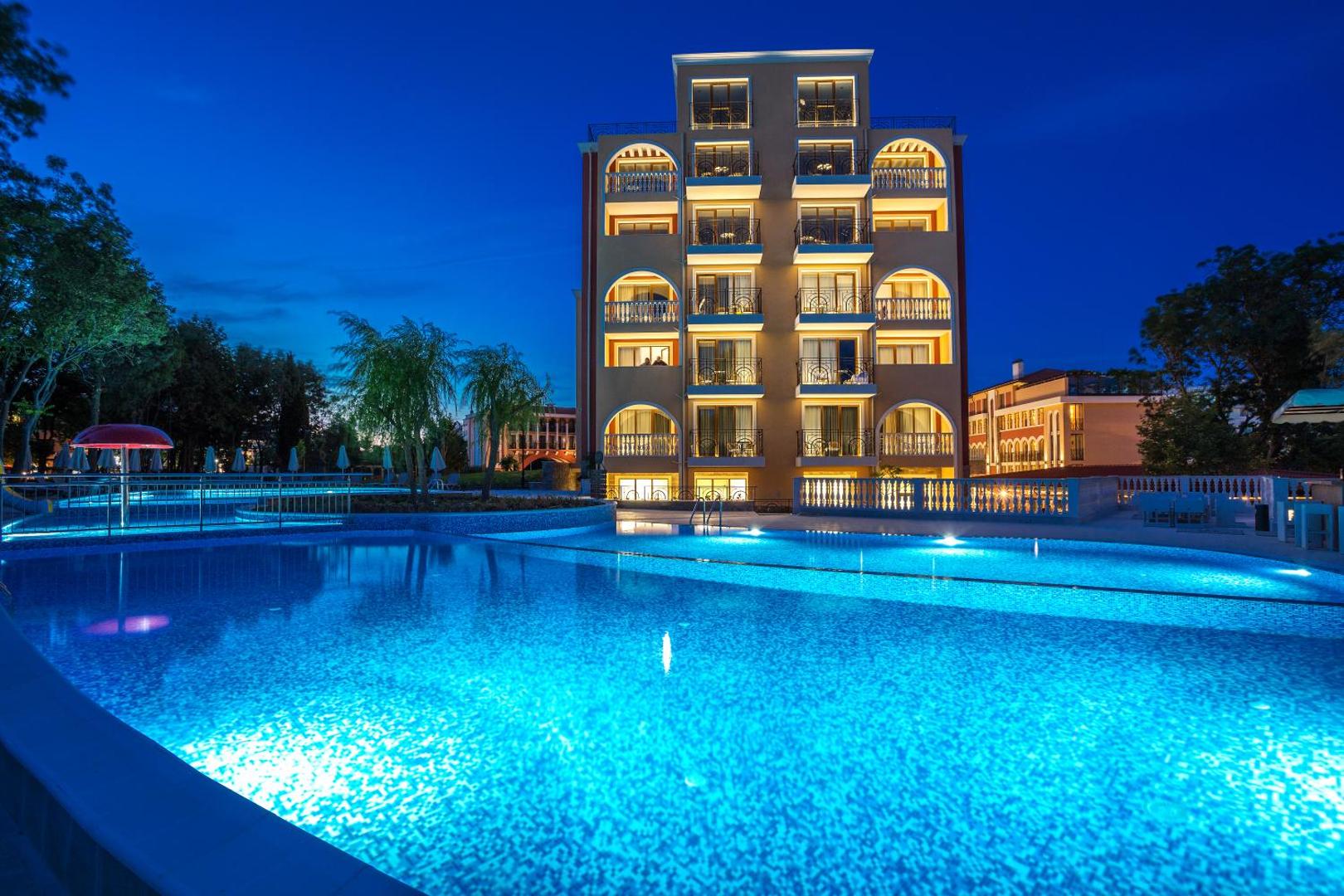 Festa Via Pontica Resort āra baseins vakarā ar izgaismotu viesnīcas fasādi Pomorijā, Bulgārijā — romantiska atmosfēra pie ūdens
