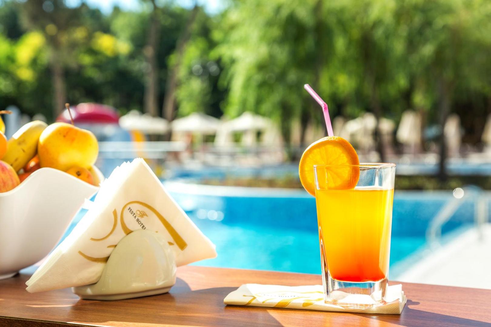 Atsvaidzinošs kokteilis ar apelsīna šķēli pie Festa Via Pontica Resort āra baseina saulainā dienā Bulgārijas piekrastē