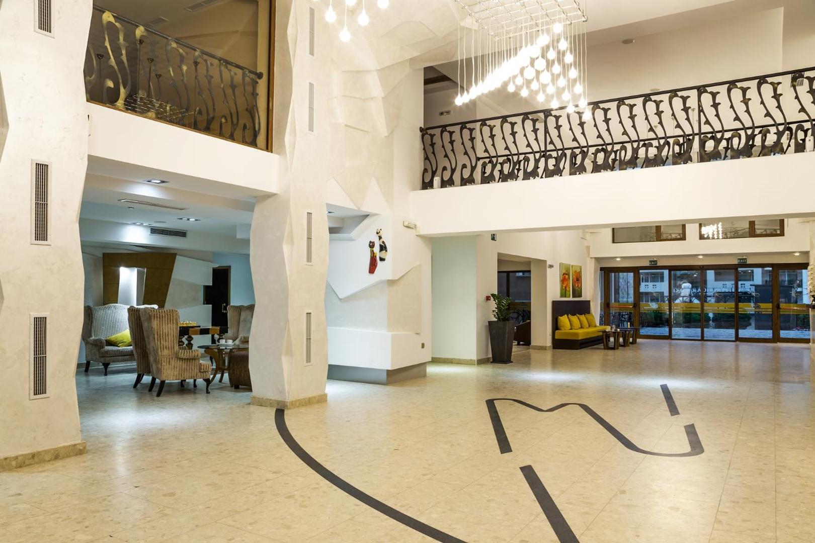 Festa Via Pontica Resort modernais un plašais vestibils ar gaišām flīžu grīdām, dizaina lustrām un atpūtas zonu Pomorijā
