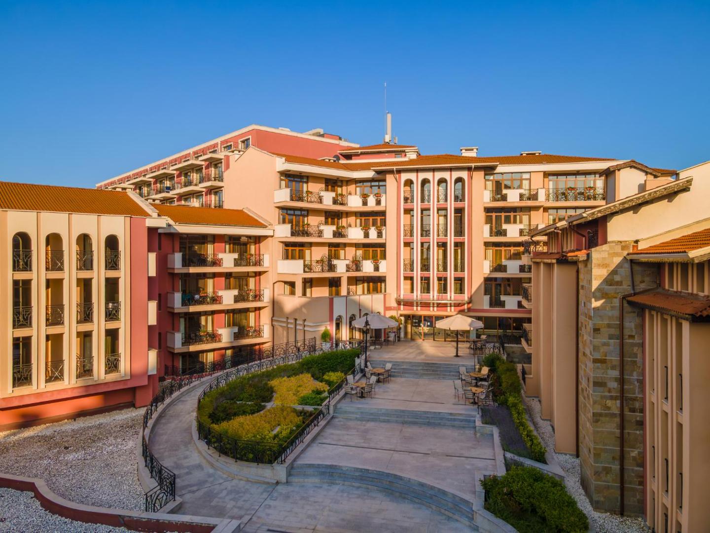 Festa Via Pontica Resort iekšpagalms ar terasēm, atpūtas zonu un klasisku arhitektūru saulrietā