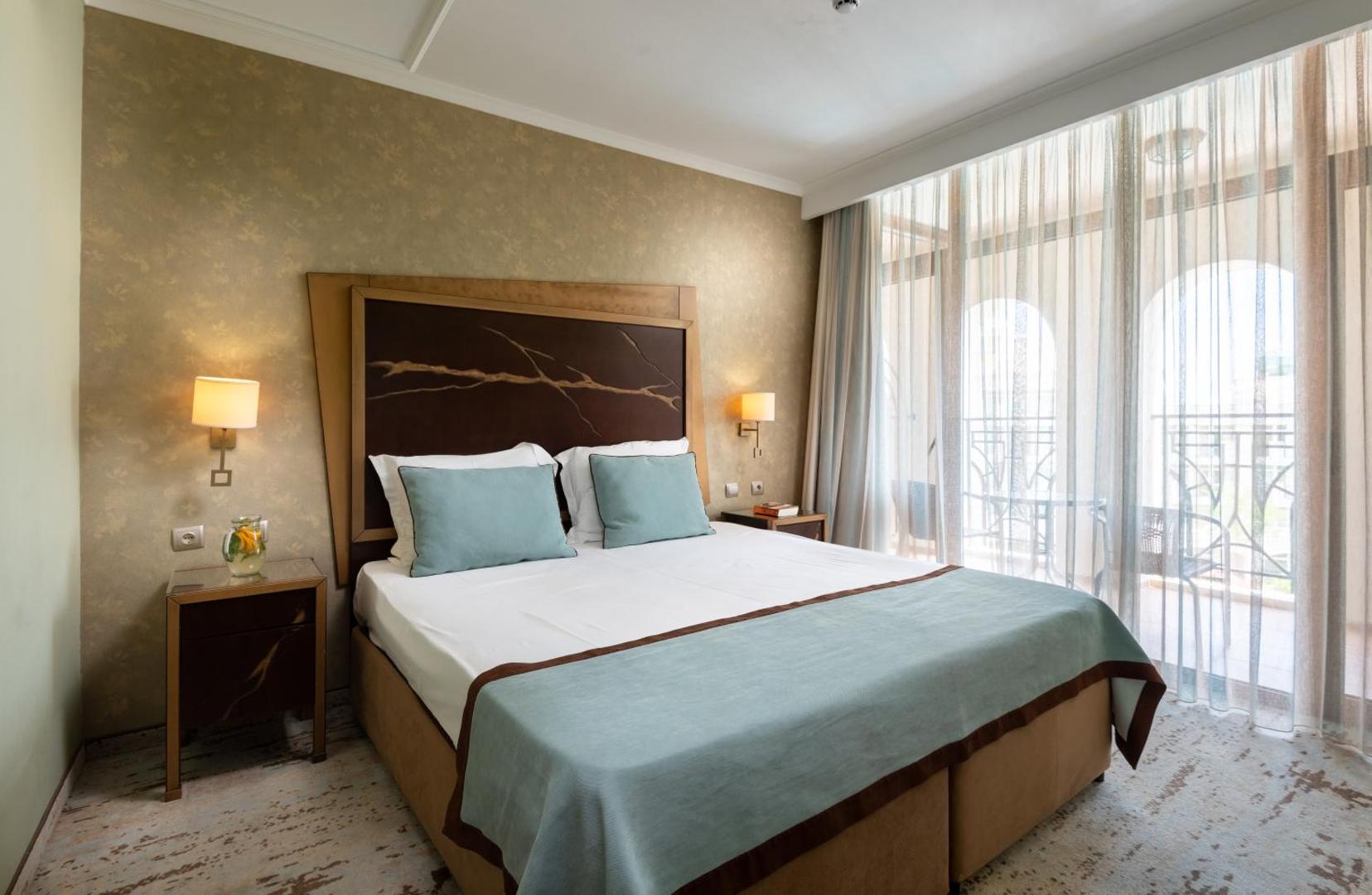 Festa Via Pontica Resort elegants guļamistabas numurs ar dekoratīvu sienas paneli virs gultas un piekļuvi balkonam