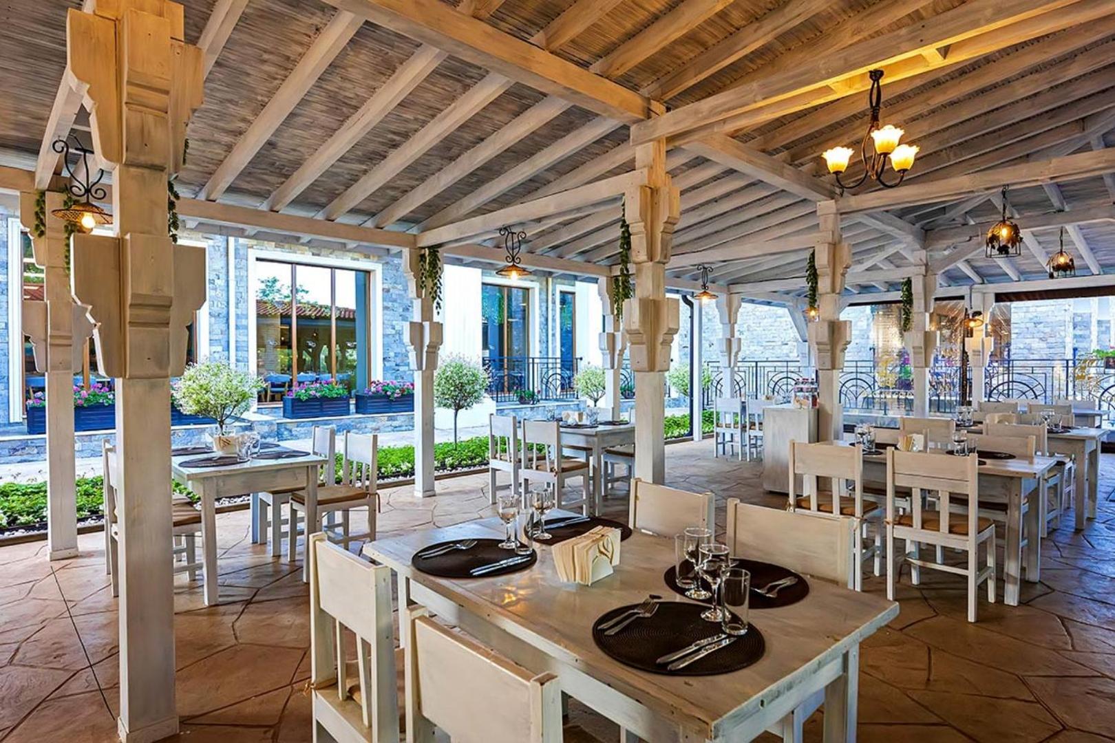 Festa Via Pontica Resort āra terase ar koka konstrukcijām, baltām mēbelēm un dekoratīviem apstādījumiem vakariņām svaigā gaisā.