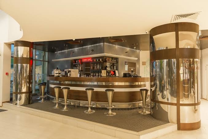 MPM Hotel Arsena modernais lobby bārs ar metāla apdares kolonnām, augstajiem krēsliem un plašu dzērienu izvēli