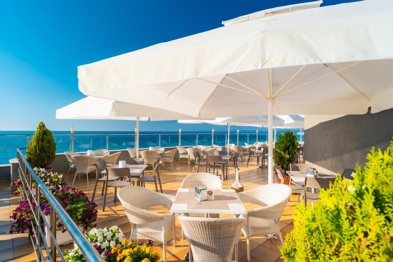 MPM Hotel Arsena āra terase ar galdiņiem, baltiem saulessargiem un panorāmas skatu uz Melno jūru