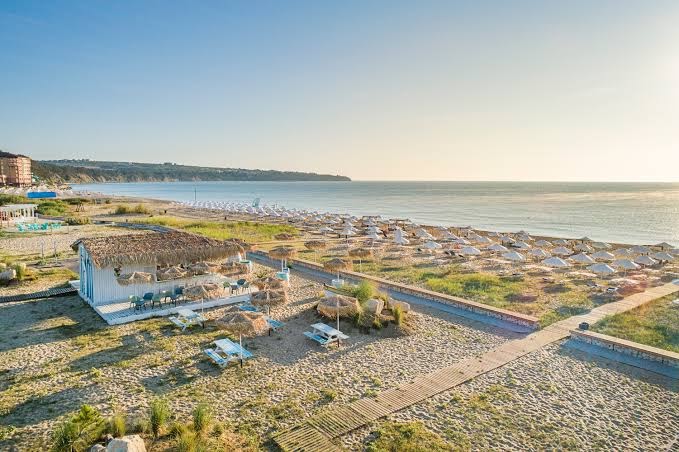 Panorāmas skats uz Sunrise Blue Magic Resort piekrasti un pludmales zonu saulrietā — koka laipas un sakopta kūrorta teritorija