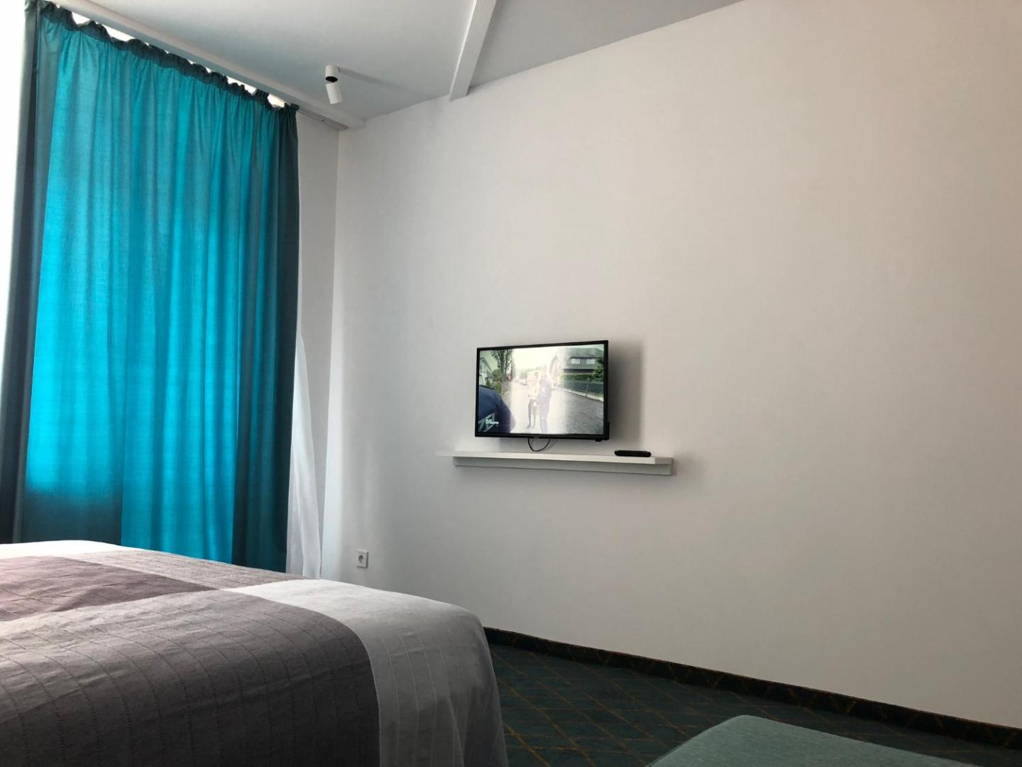 Televizors pie sienas Sunrise Blue Magic Resort viesnīcas numurā ar ziliem aizkariem un modernu apgaismojumu