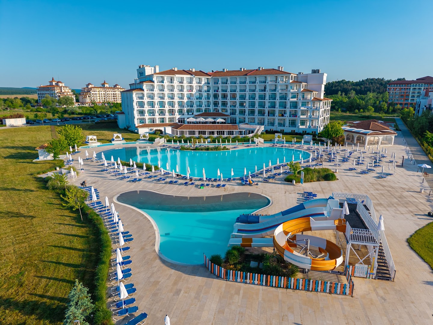 Sunrise Blue Magic Resort āra baseinu komplekss ar ūdens slidkalniņiem bērniem, sauļošanās krēsliem un galveno viesnīcas korpusu fonā