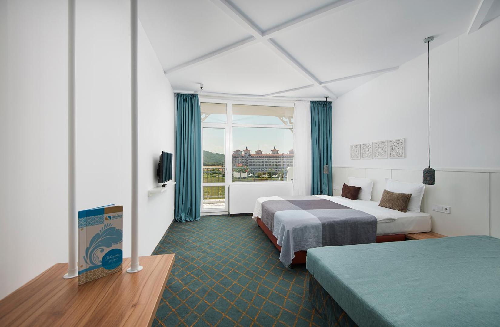 Sunrise Blue Magic Resort gaišs numurs ar divguļamo gultu, dīvānu un skatu pa logu uz kūrorta teritoriju Obzorā