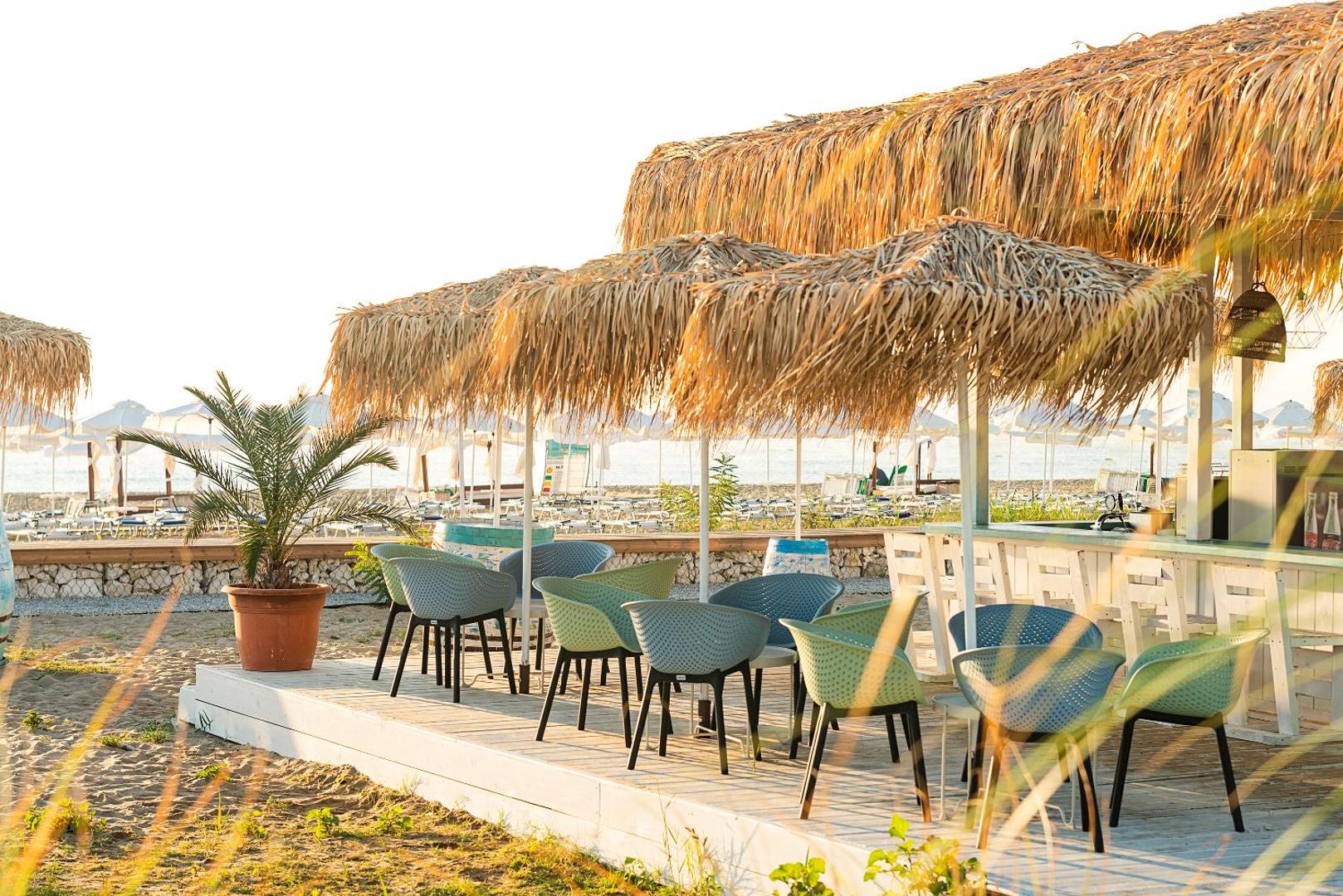 Sunrise Blue Magic Resort pludmales bārs ar salmu jumtu un stilīgiem krēsliem — atpūtas zona smiltīs ar skatu uz jūru
