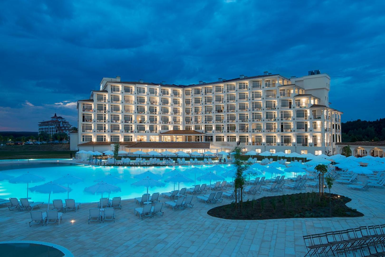 Sunrise Blue Magic Resort viesnīcas ēka un izgaismots āra baseins vakarā Obzorā, Bulgārijā — atpūtas zona ar saulessargiem