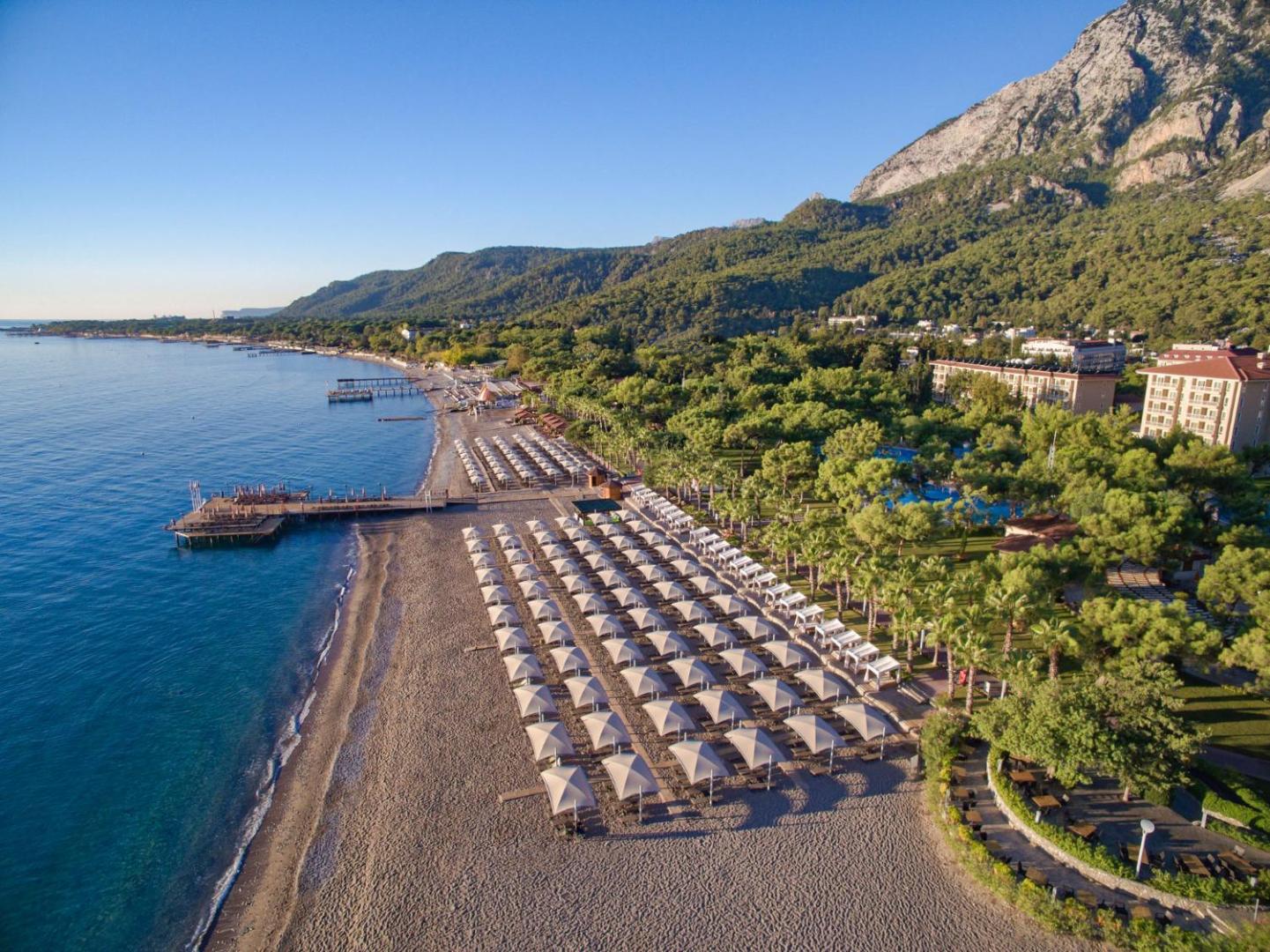 Akka Antedon viesnīcas teritorija no putna lidojuma — plaša oļu pludmale, kalnu fons, priežu dārzs un viesnīcas korpusi Kemeras reģionā