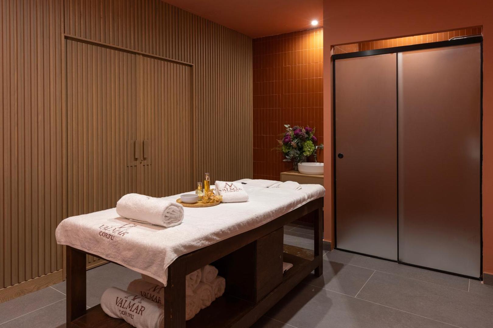 Valmar Corfu spa centra masāžas telpa ar koka paneļu sienām, masāžas galdu un relaksējošu apgaismojumu