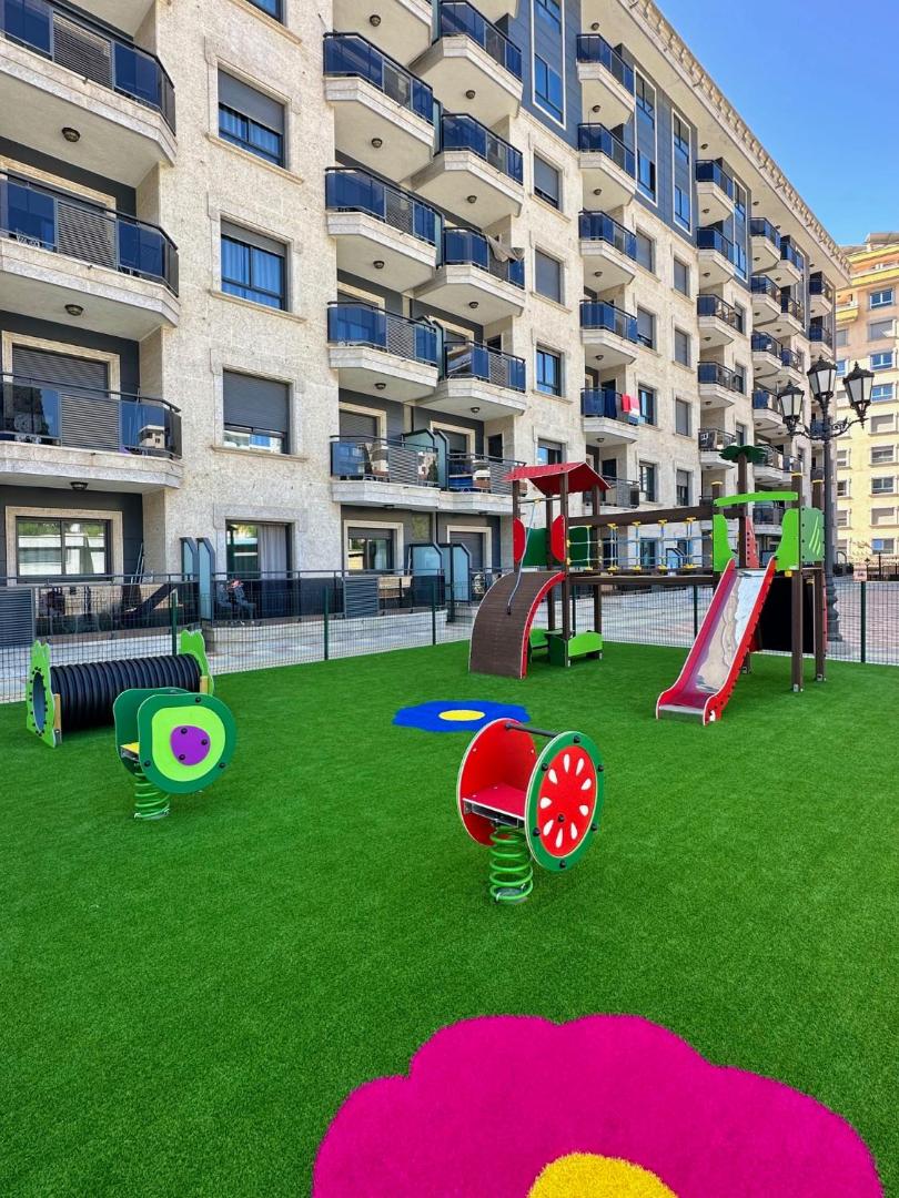 Apartamentos Nuria Sol bērnu rotaļu laukums ar krāsainām atrakcijām un mākslīgo zālienu Fuengirolā, Spānijā pie viesnīcas ēkas