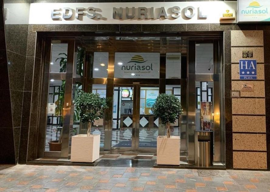 Apartamentos Nuria Sol 3* apartamentu viesnīcas ieeja naktī Fuengirolā — izgaismota izkārtne un stikla fasāde ar dekoratīviem kokiem