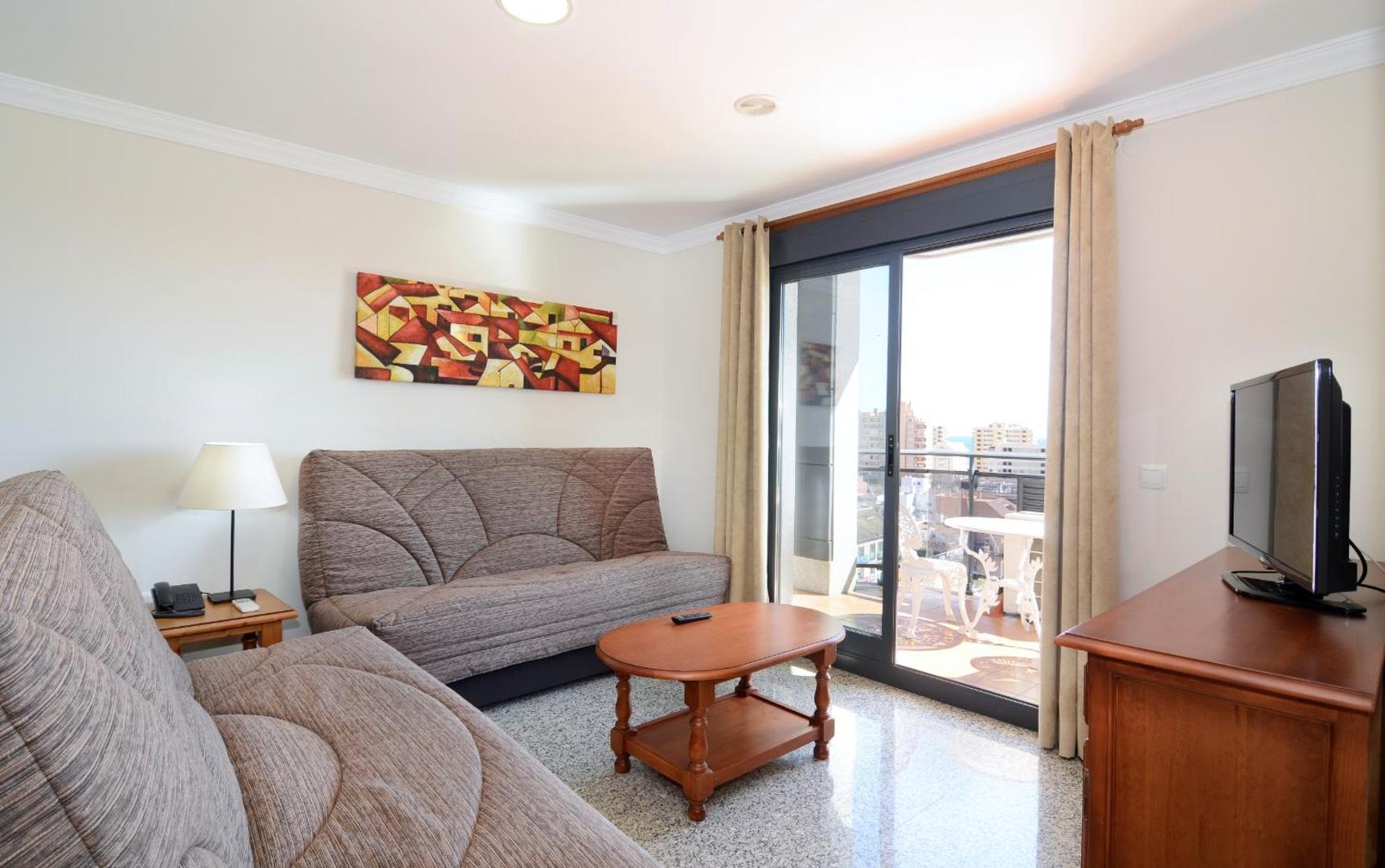 Apartamentos Nuria Sol viesistaba ar diviem dīvāniem, kafijas galdiņu un izeju uz balkonu ar skatu uz pilsētu