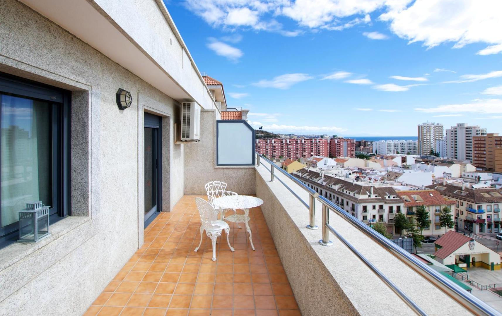 Apartamentos Nuria Sol plašs balkons ar baltu galdu un krēsliem, no kura paveras skats uz Fuengirolas pilsētu un jūru