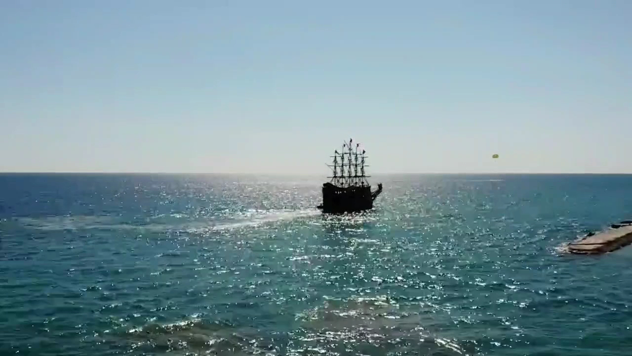 Stilizēts pirātu kuģis jūrā pie Eftalia Ocean viesnīcas krasta saules atspīdumos — populāra izklaide tūristiem Alanjas piekrastē