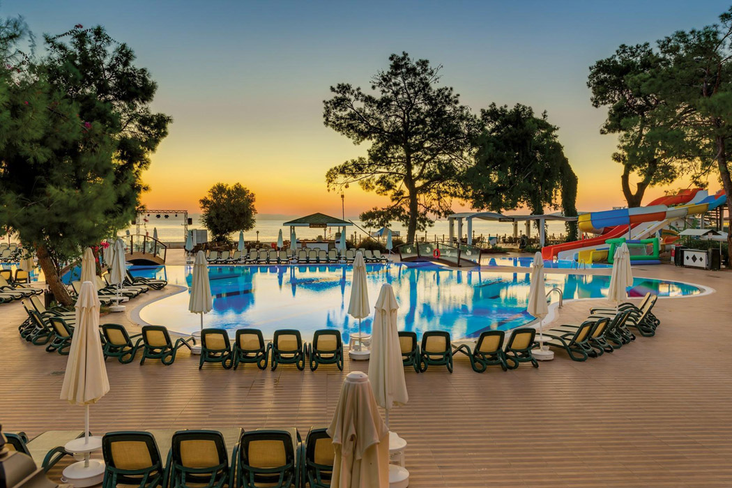 Saulrieta skats uz Crystal Aura Beach Resort & Spa āra baseinu, pludmales saulessargiem un jūras piekrasti fonā