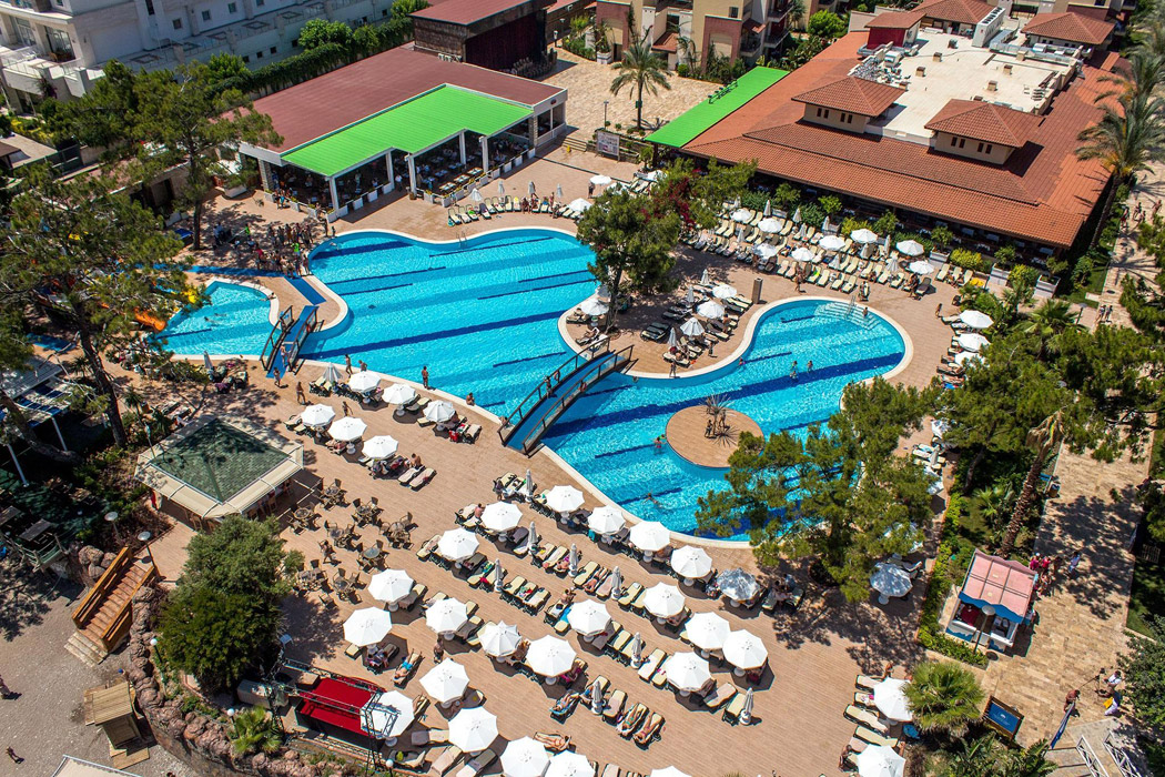 Crystal Aura Beach Resort & Spa galvenā baseina zona ar tiltiņu, saulessargiem un restorāna terasi saulainā dienā