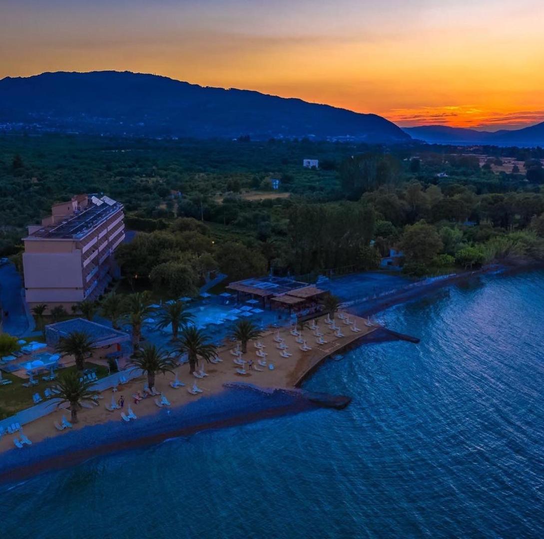 Long Beach Resort skats uz pludmali un viesnīcas ēku saulrieta laikā — oranžas debesis virs kalniem un jūras piekrastes