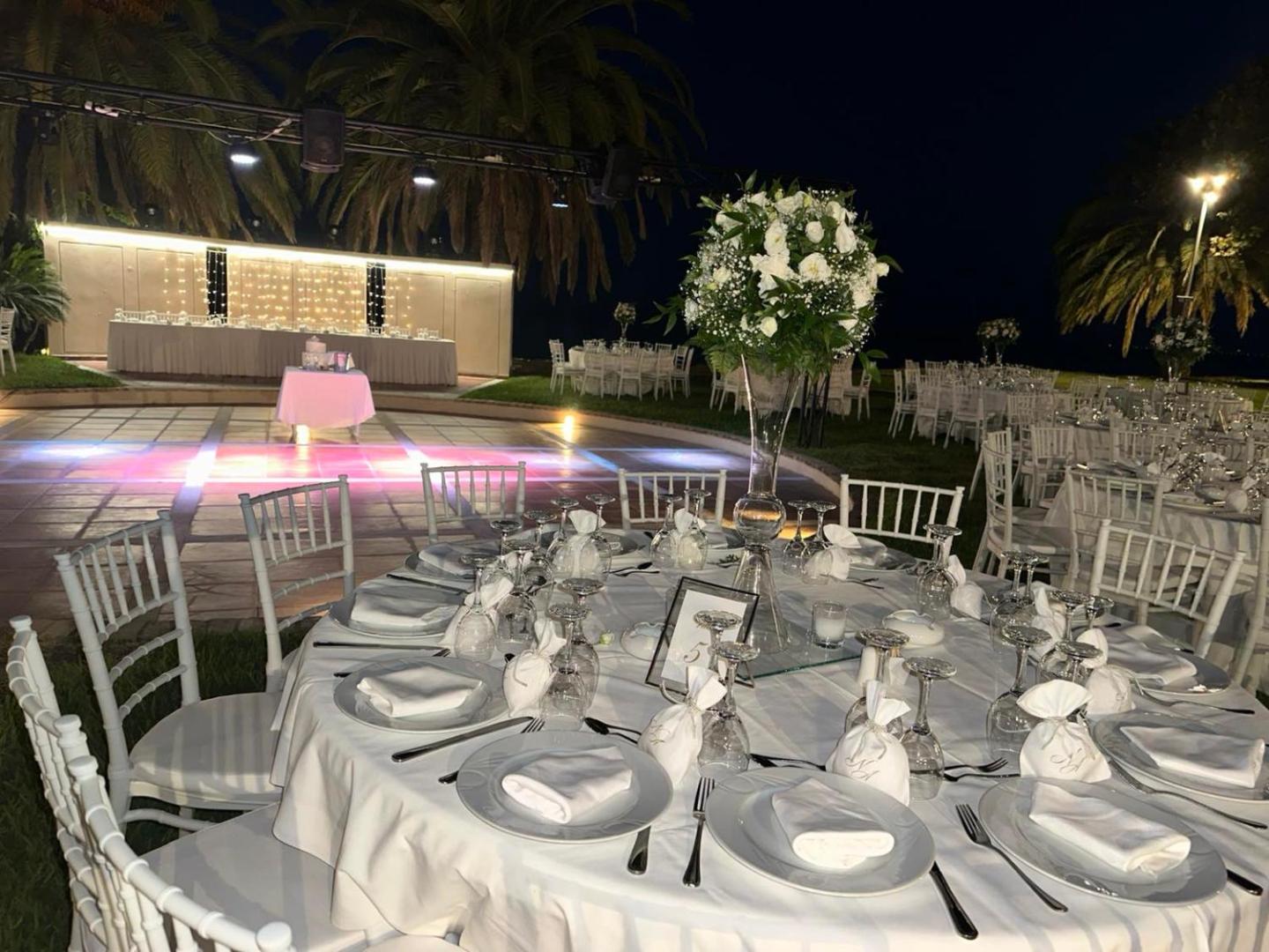 Long Beach Resort svinību vieta vakarā Krētā — eleganti klāti apaļie galdi ar baltiem krēsliem pie izgaismotas deju grīdas un palmām
