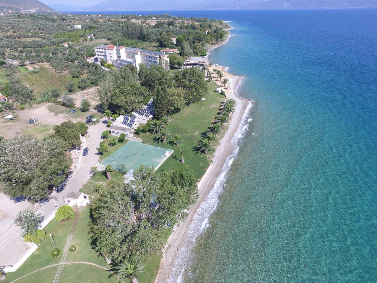 Long Beach Resort panorāmas skats uz garu oļu pludmali, dzidru jūras ūdeni un viesnīcas teritoriju Grieķijas piekrastē
