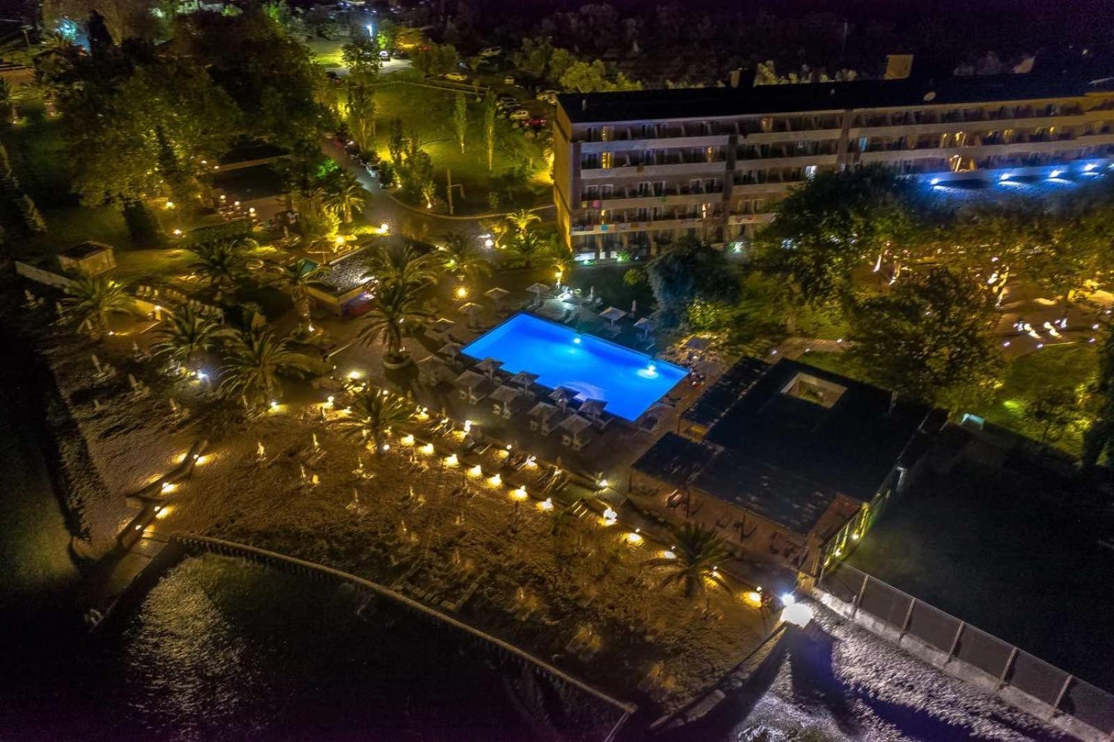 Long Beach Resort nakts skats no augšas uz izgaismotu baseinu, viesnīcas korpusu un pludmales zonu Grieķijā