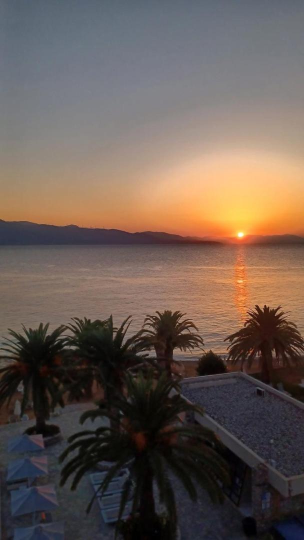 Saulriets virs jūras un kalniem, skatoties no Long Beach Resort teritorijas caur palmu galotnēm vakara gaismā.