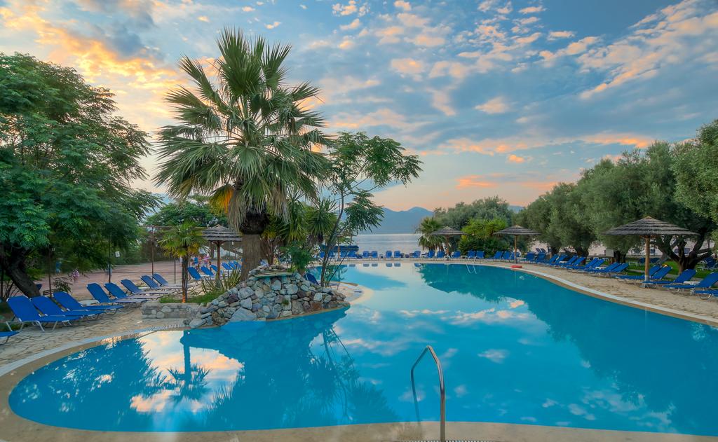 Florida Blue Bay āra baseins saulrieta laikā ar palmām, atpūtas krēsliem un mākoņainām debesīm, kas atspoguļojas ūdenī