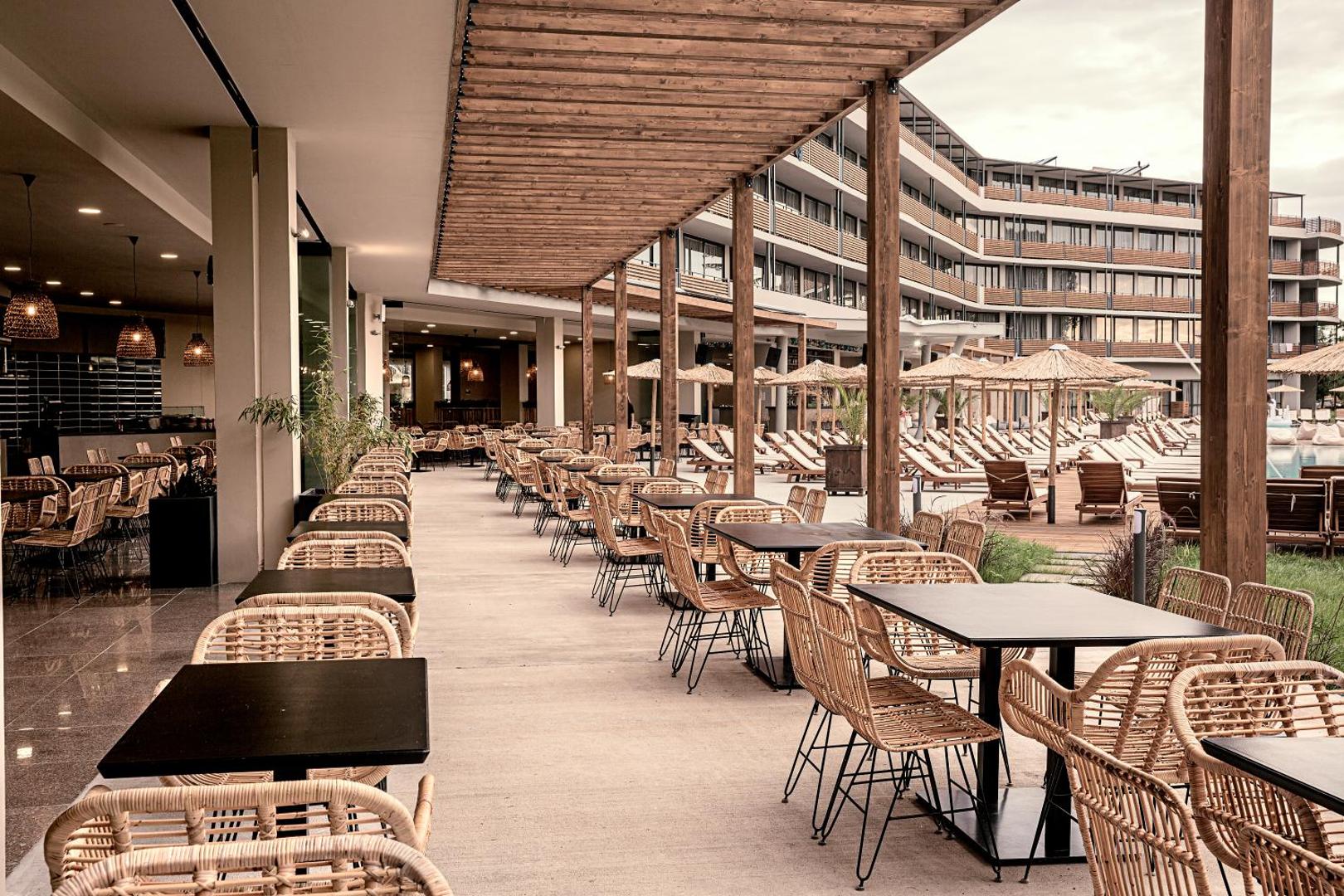 Sunny Beach Club viesnīcas restorāna āra terase ar pītiem krēsliem un koka nojumi, skats uz baseina zonu.