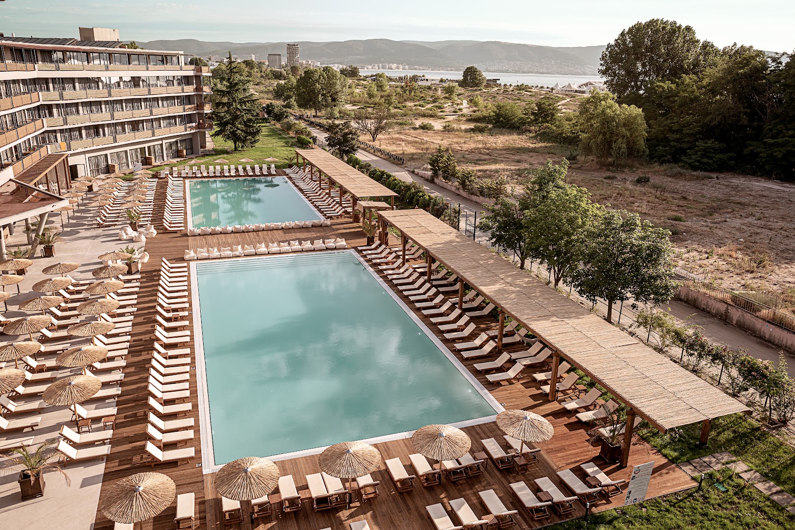 Sunny Beach Club viesnīcas āra baseinu zona Saulainajā krastā, Bulgārijā — divi lieli baseini ar sauļošanās krēsliem, saulessargiem un koka terasi