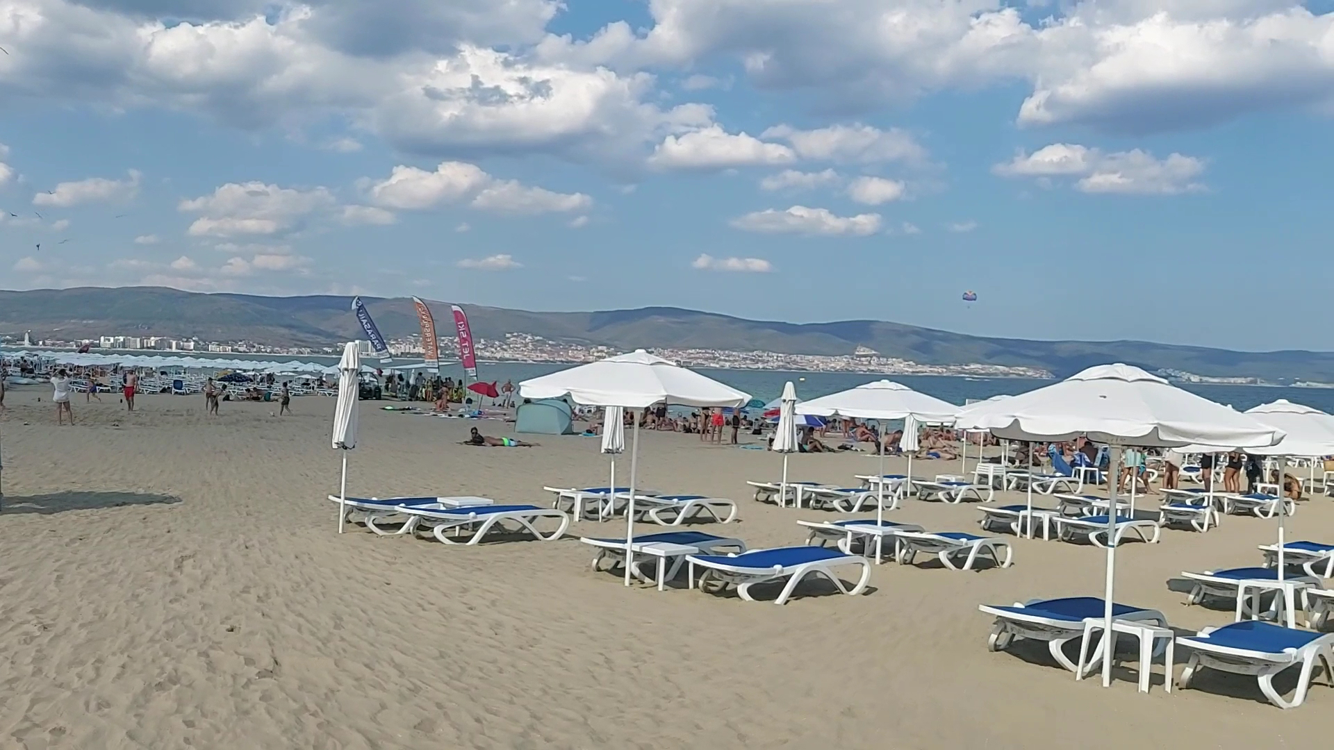 Sunny Beach Club privātā pludmale Saulainajā krastā, Bulgārijā – balti saulessargi un zili sauļošanās krēsli plašā smilšu piekrastē.