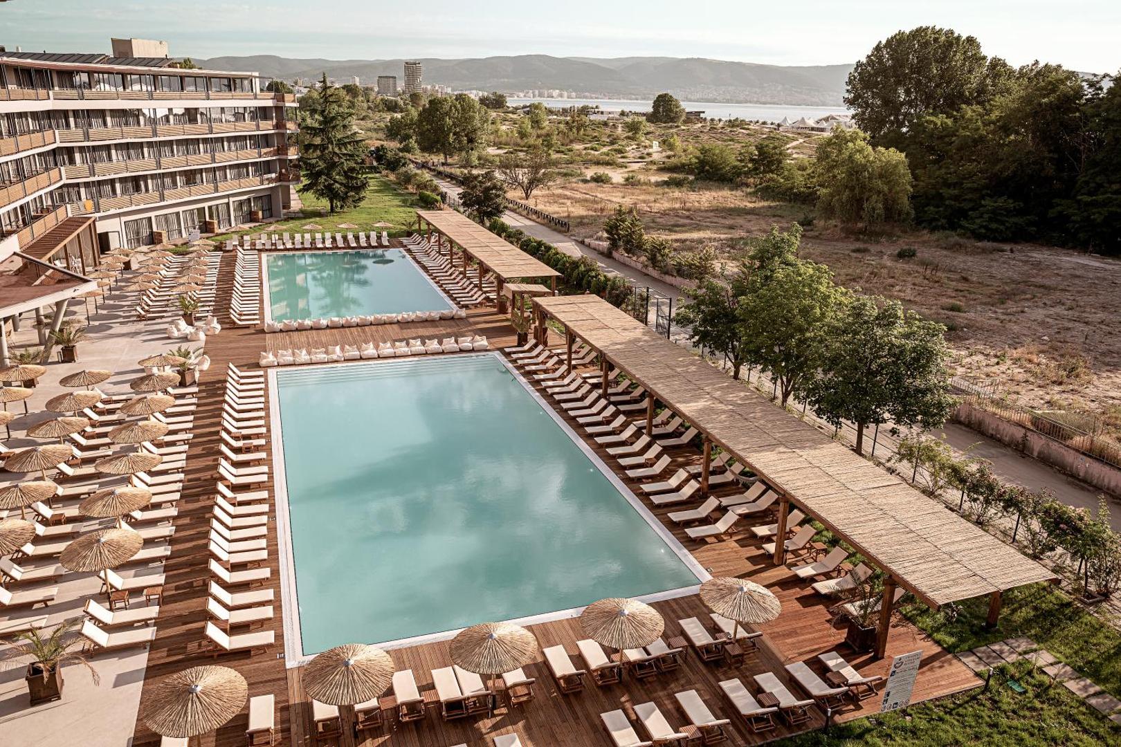 Sunny Beach Club viesnīcas kopskats ar diviem lieliem āra baseiniem, sauļošanās krēsliem un skatu uz jūru Saulainajā krastā, Bulgārijā.