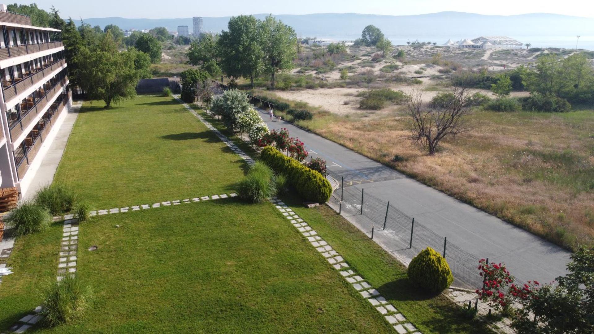 Sunny Beach Club teritorijas skats uz kāpām un jūras piekrasti Saulainajā krastā — zaļš zālājs un gājēju celiņš