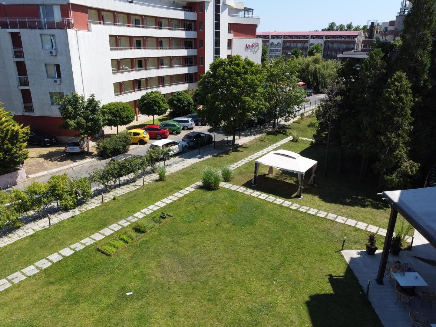 Skats no augšas uz Sunny Beach Club viesnīcas ēku un zaļo pagalmu ar zālāju, koku rindu un pastaigu celiņiem