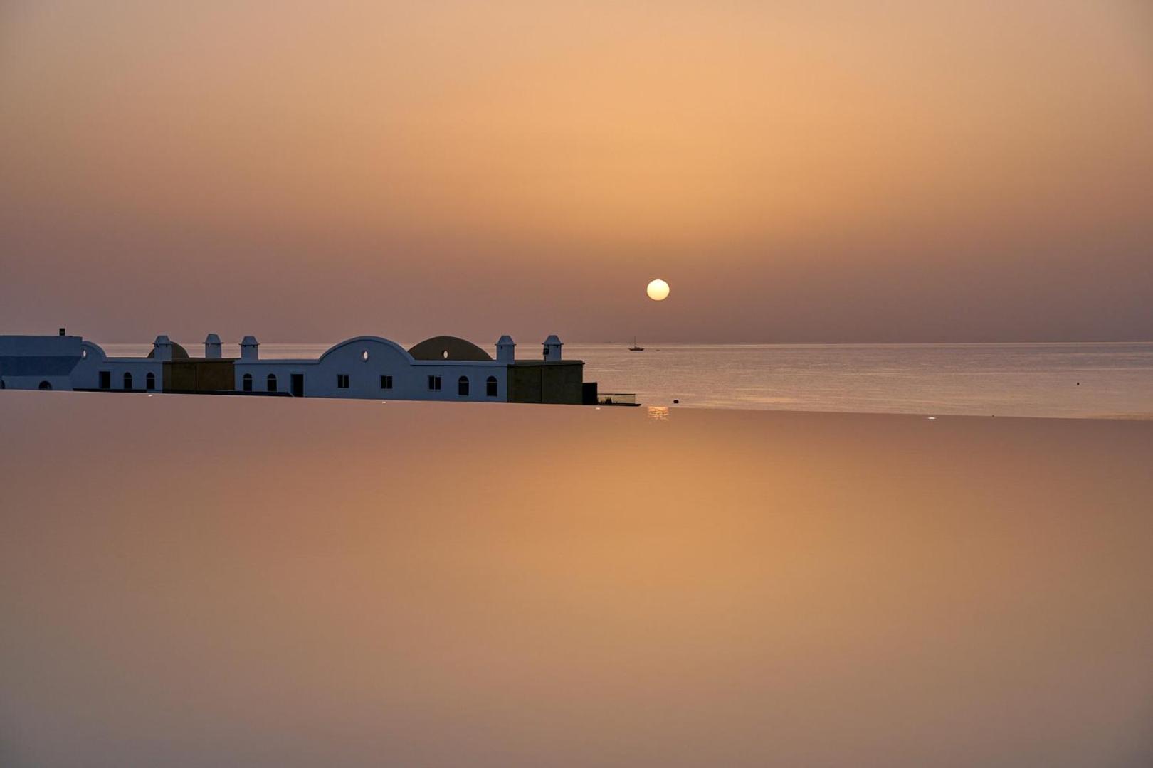 Lindos Grand Resort & Spa bezmalas baseina skats uz saulrietu un viesnīcas arhitektūru Rodas salā, Grieķijā — mierpilna vakara atmosfēra