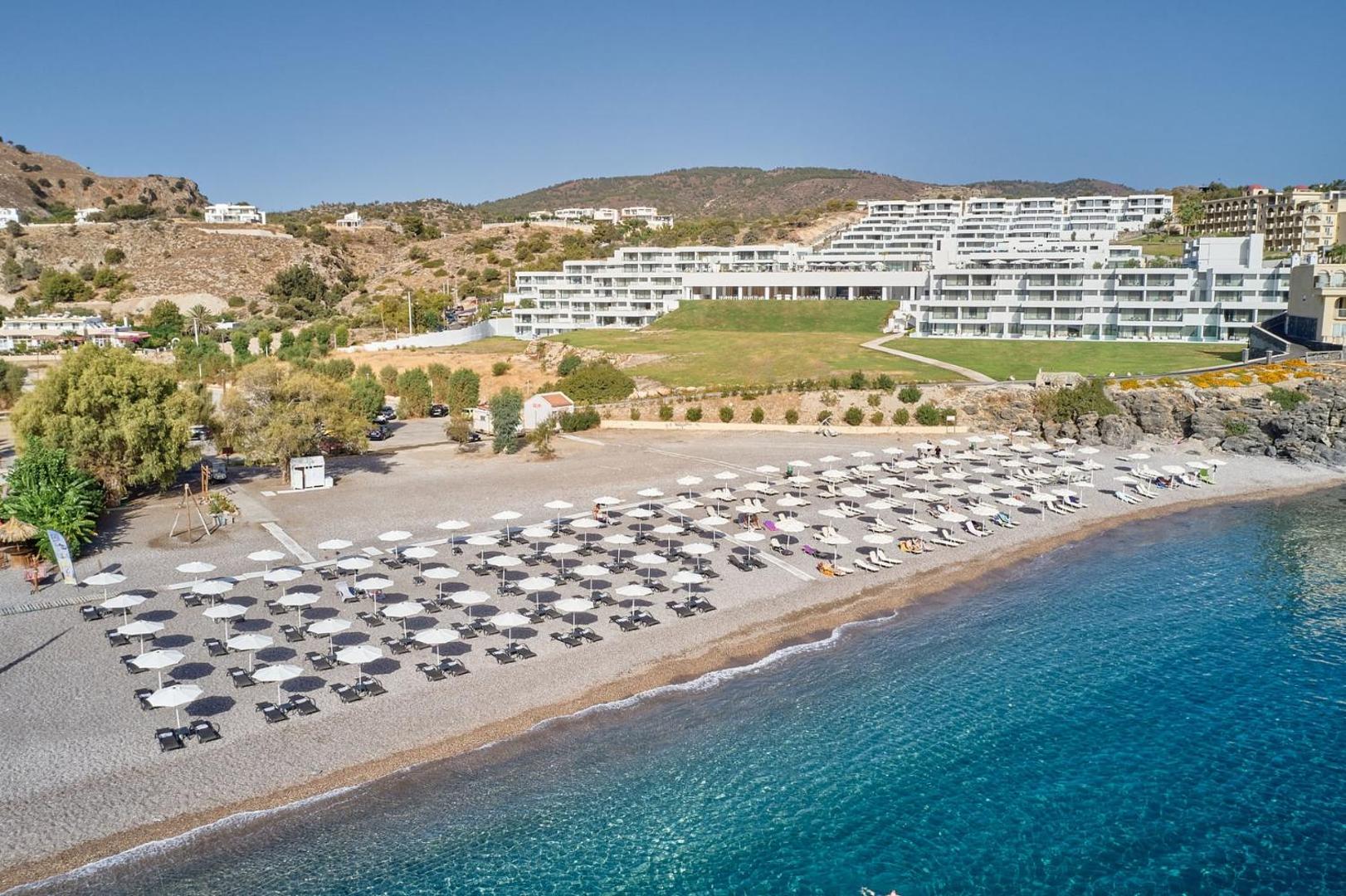 Lindos Grand Resort & Spa privātā pludmale ar saulessargiem un gultām pie dzidri zilās Vidusjūras Rodas piekrastē