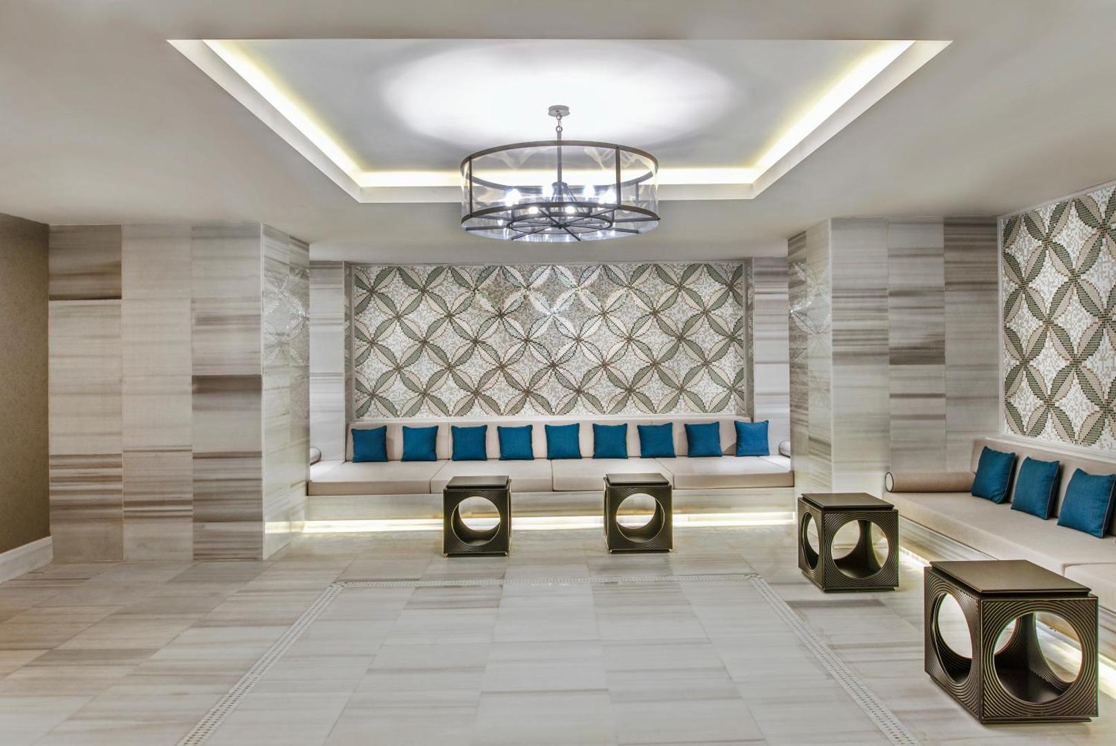 Regnum Carya spa centra atpūtas telpa ar mīkstiem dīvāniem, dekoratīviem spilveniem un mozaīkas sienas paneli mierīgai gaisotnei
